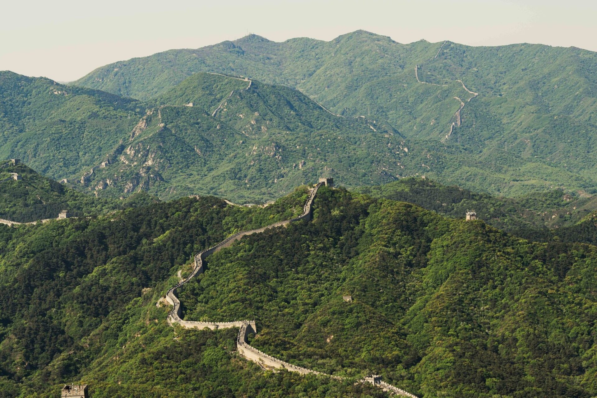 Aerial view of the Great Wall of China extending over lush, green hills in Beijing during spring.