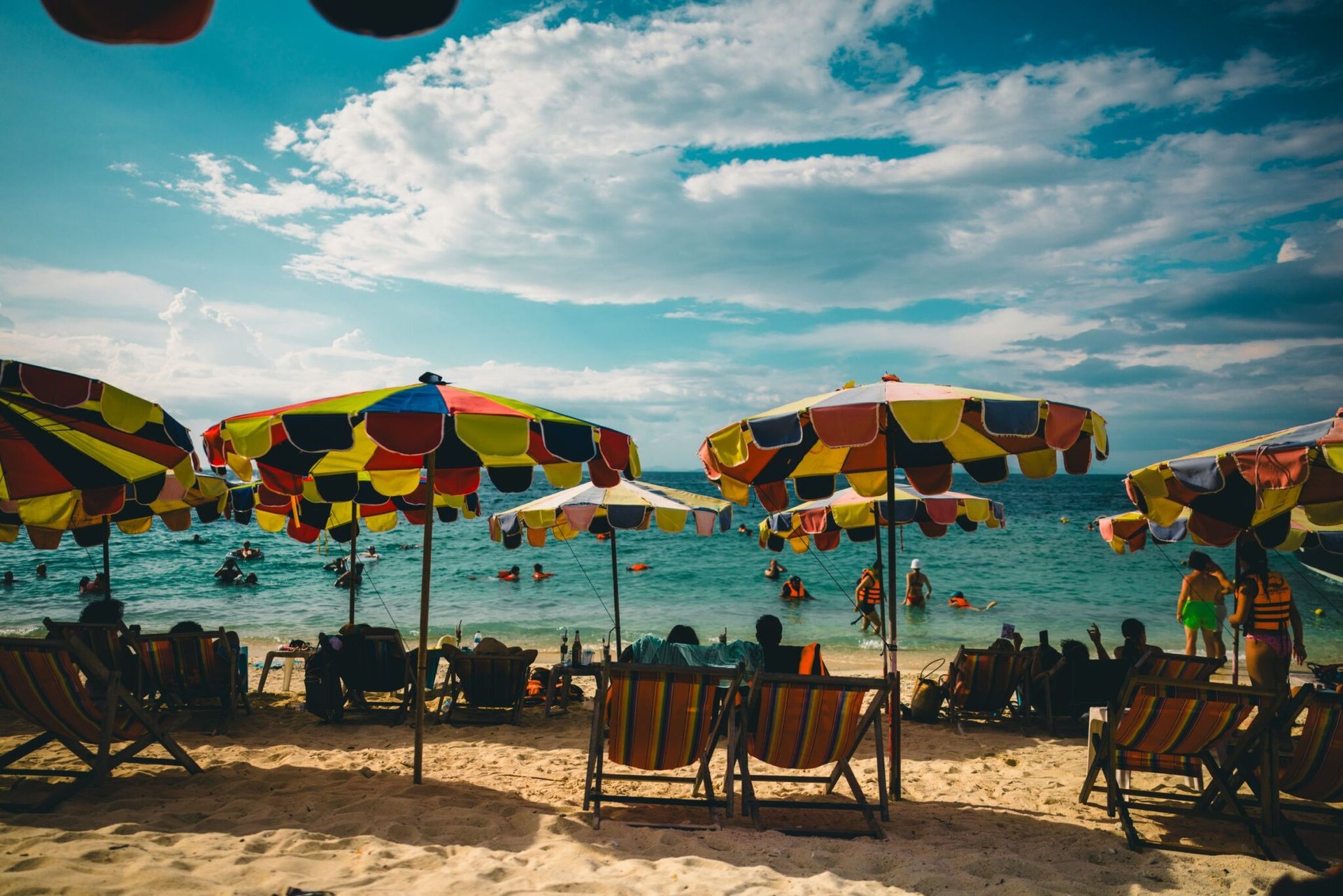 Colorful umbrellas and loungers on a lively beach in Phuket, Thailand, during a sunny day.