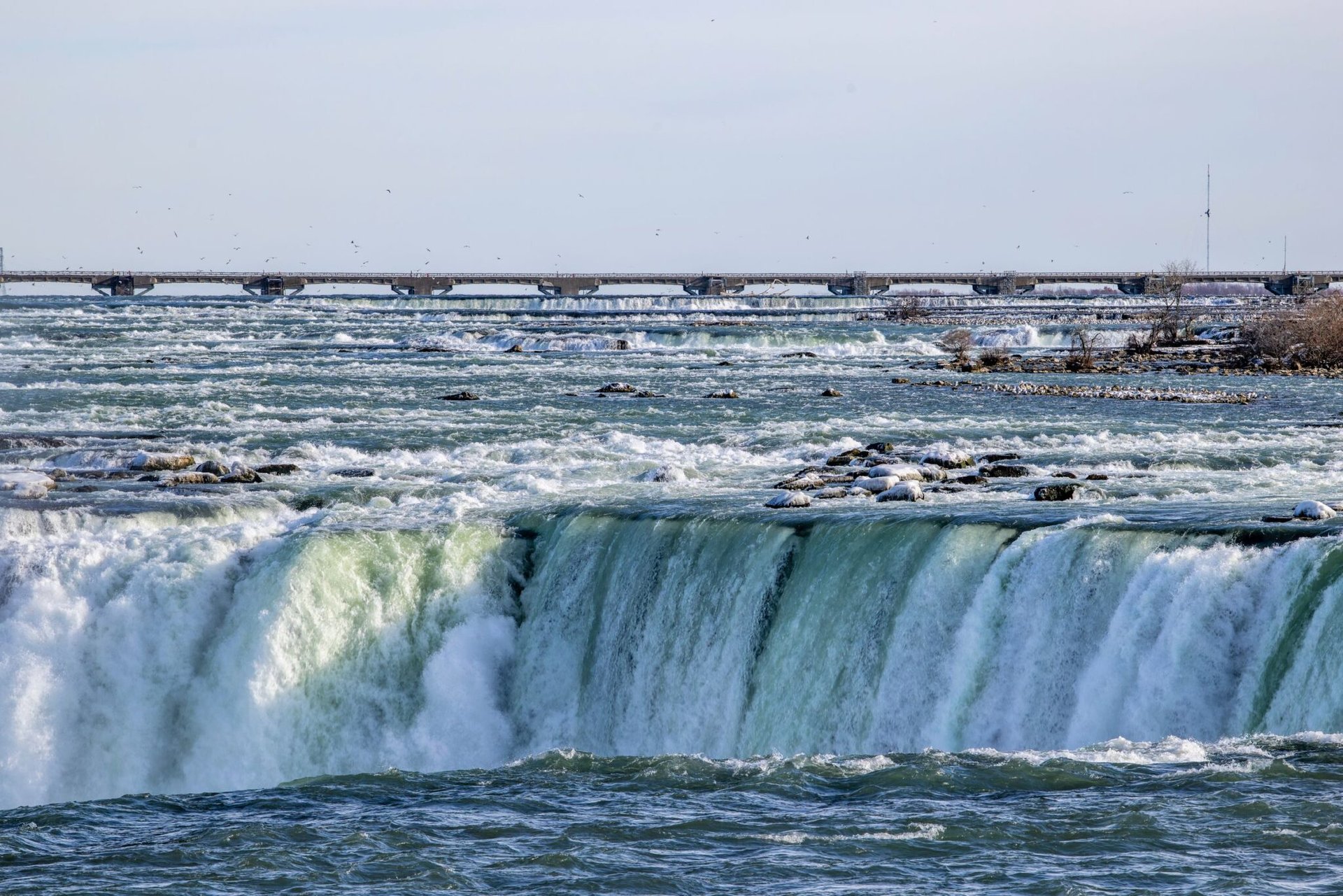 Scenic view of Niagara Falls with cascading water and a distant bridge under a clear sky.