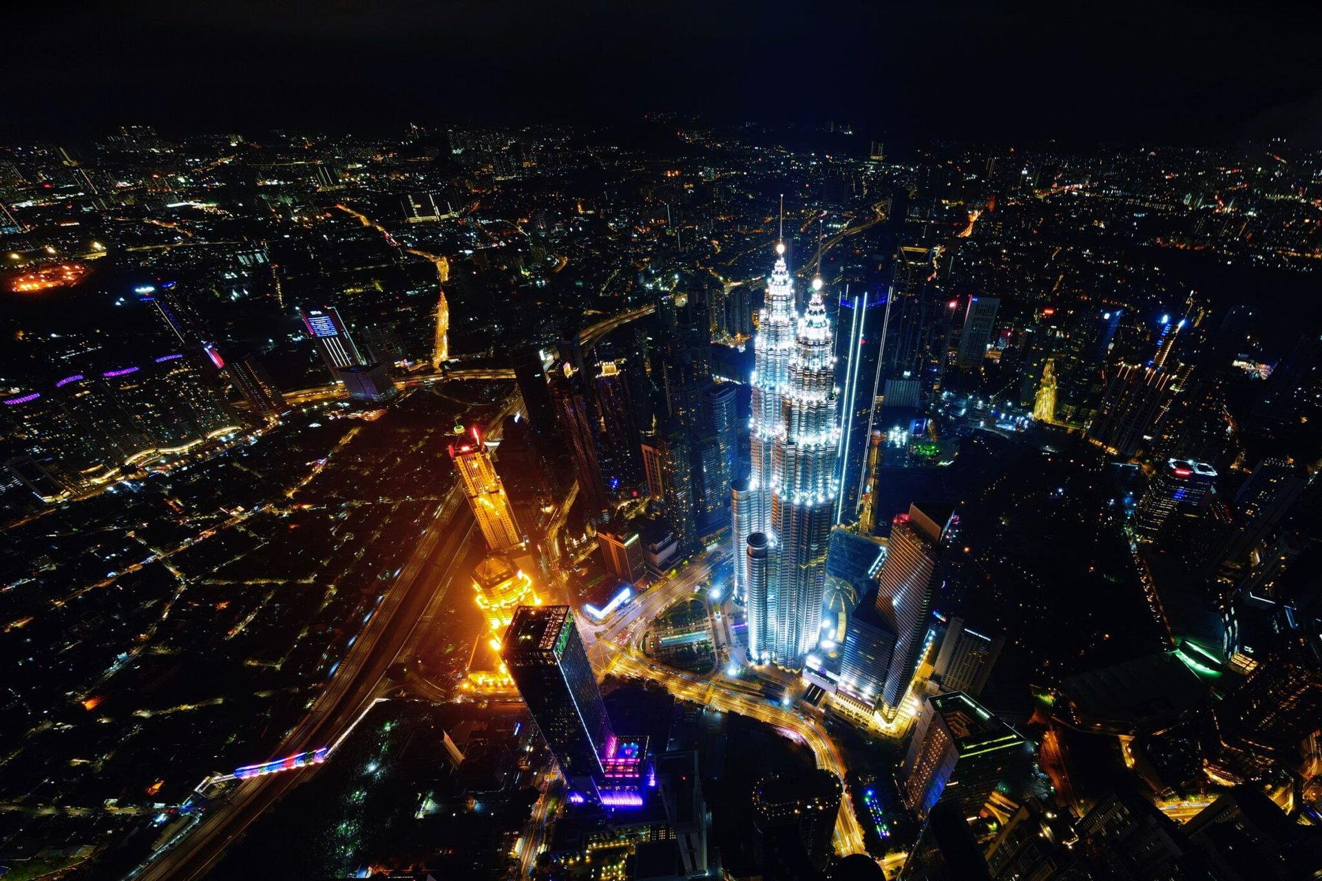 Aerial view of Kuala Lumpur cityscape at night, featuring the illuminated Petronas Twin Towers.