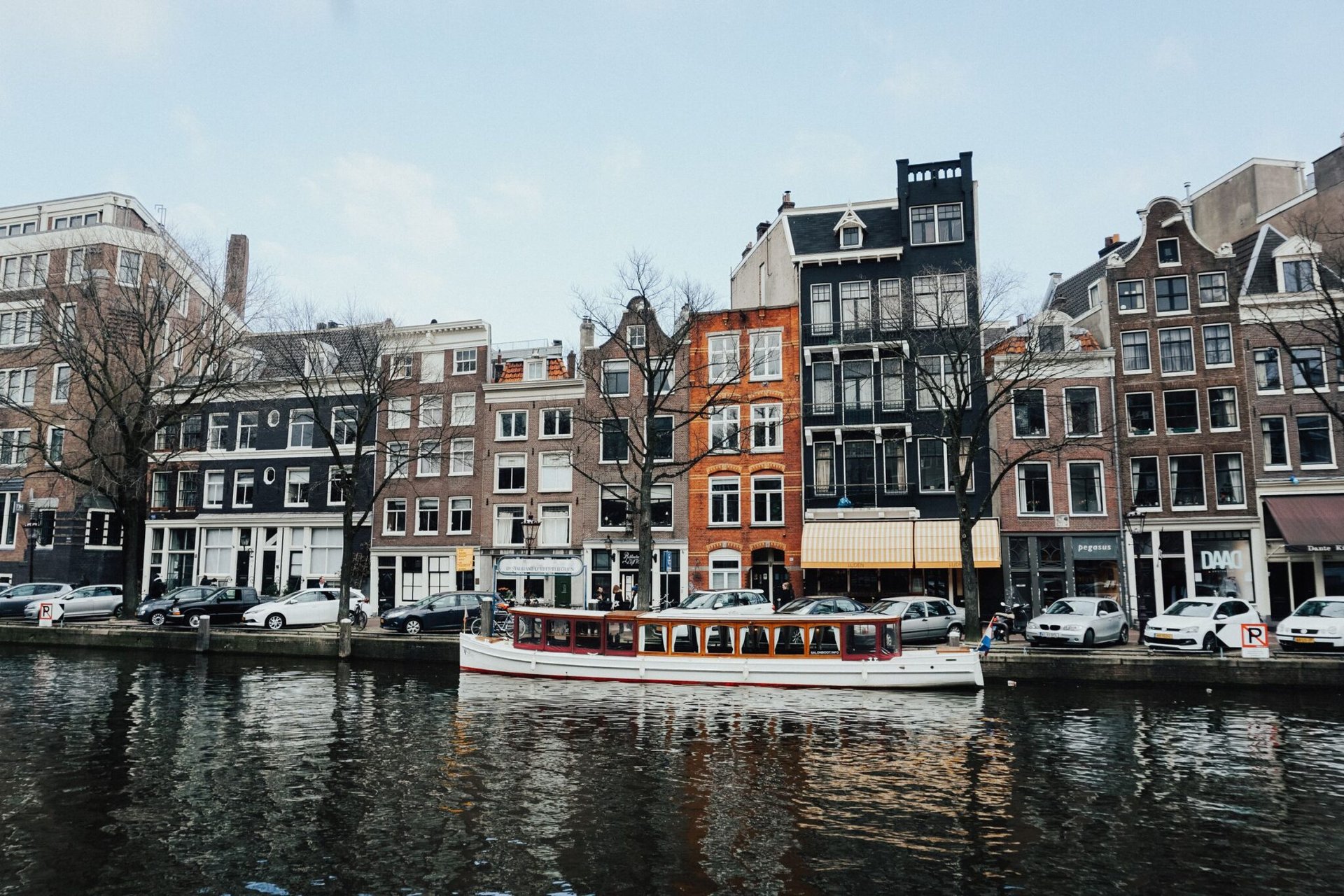 Charming Amsterdam canal scene with classic Dutch architecture and a boat cruising on the water.