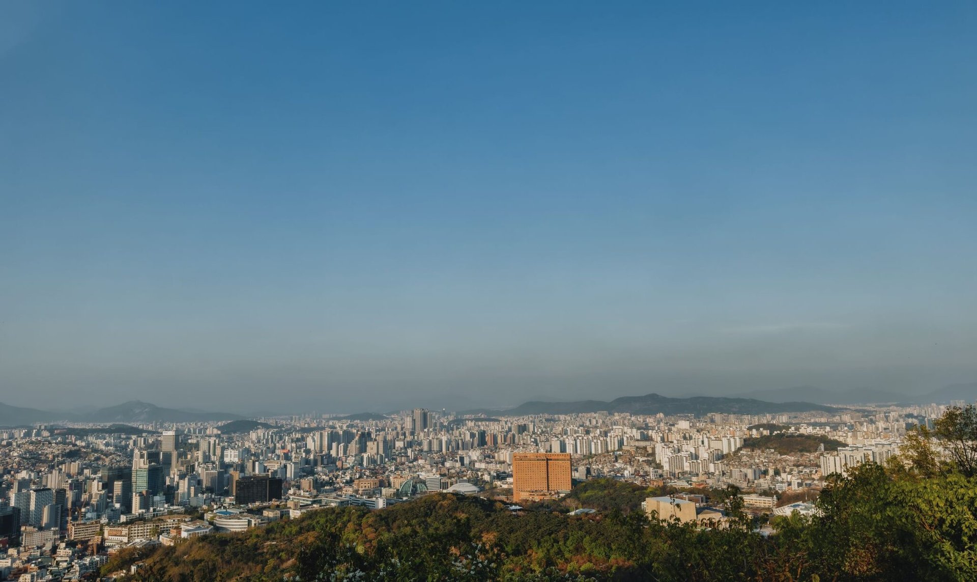 Expansive view of Seoul's skyline from a hilltop with clear blue sky.