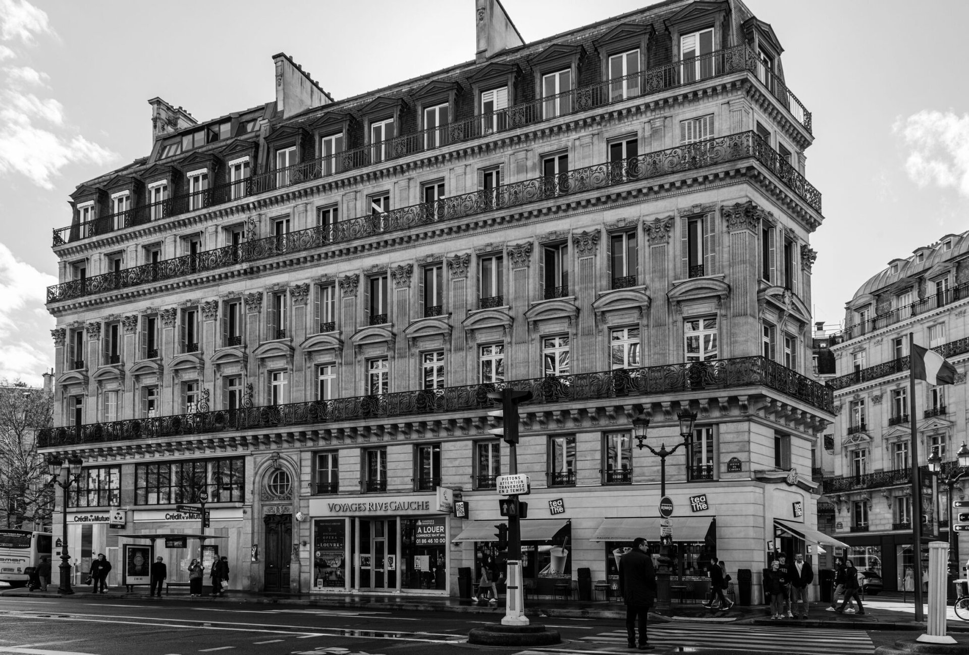 Black and white photo of a classic Parisian building located on a busy street corner in Paris, France.