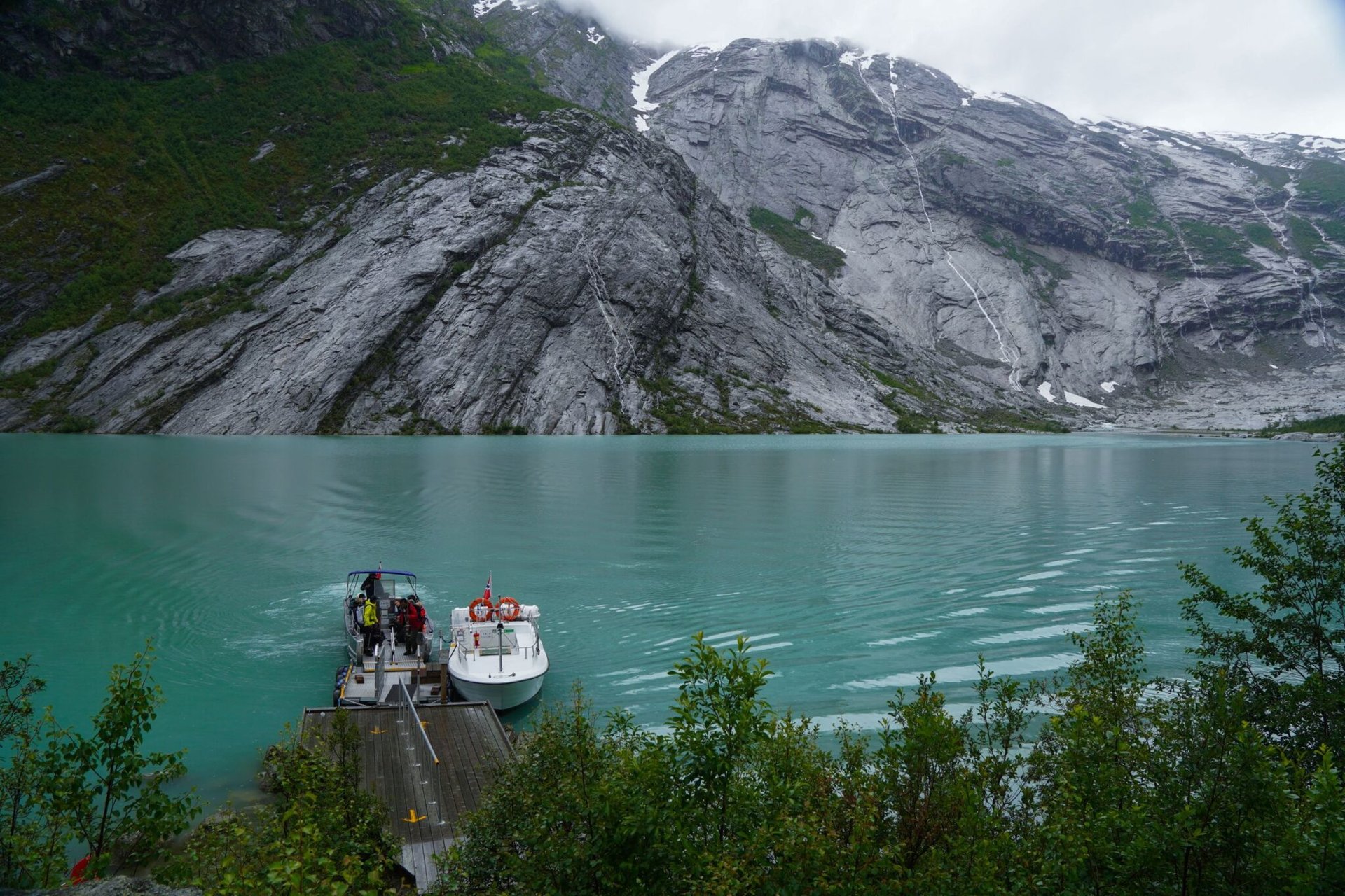 Stunning turquoise water with a boat docked at a fjord surrounded by rugged cliffs in Norway.