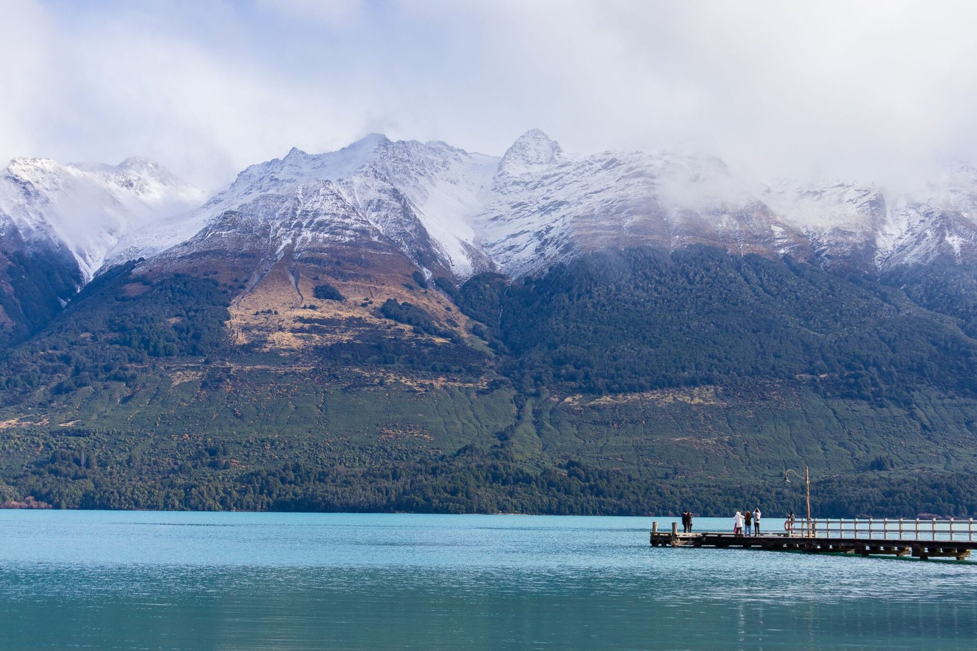 Tranquil scene of a dock on Lake Wakatipu with majestic snow-capped mountains in Queenstown, New Zealand.