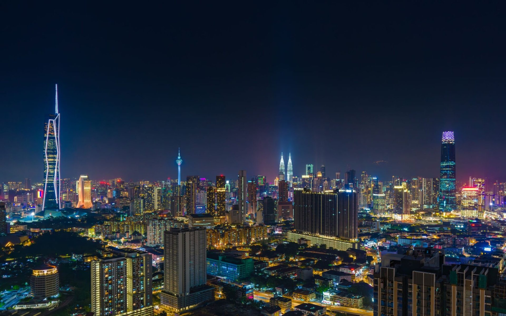 A vibrant night view of Kuala Lumpur's skyline featuring the iconic Petronas Towers.