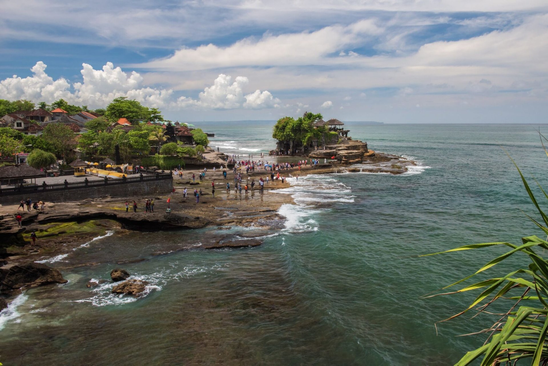 A breathtaking view of Tanah Lot Temple surrounded by the ocean in Bali, Indonesia with tourists exploring the area.