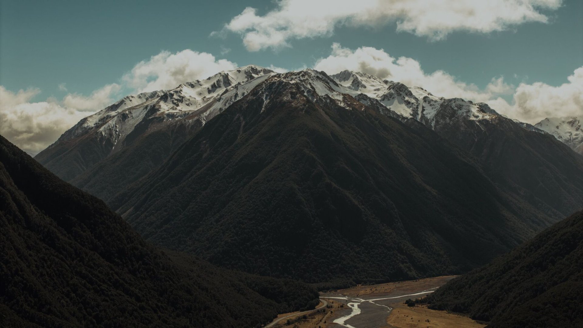A stunning view of the Southern Alps in New Zealand, showcasing snow-capped mountains and a winding river below.