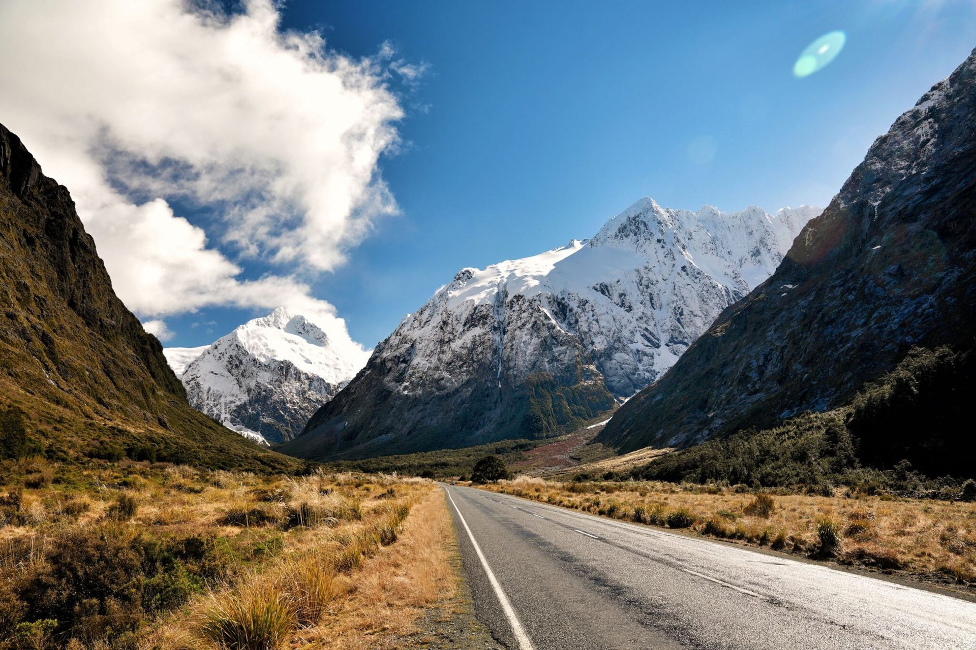 Sunlit scenic road through snowy mountains in Southland Region, New Zealand.