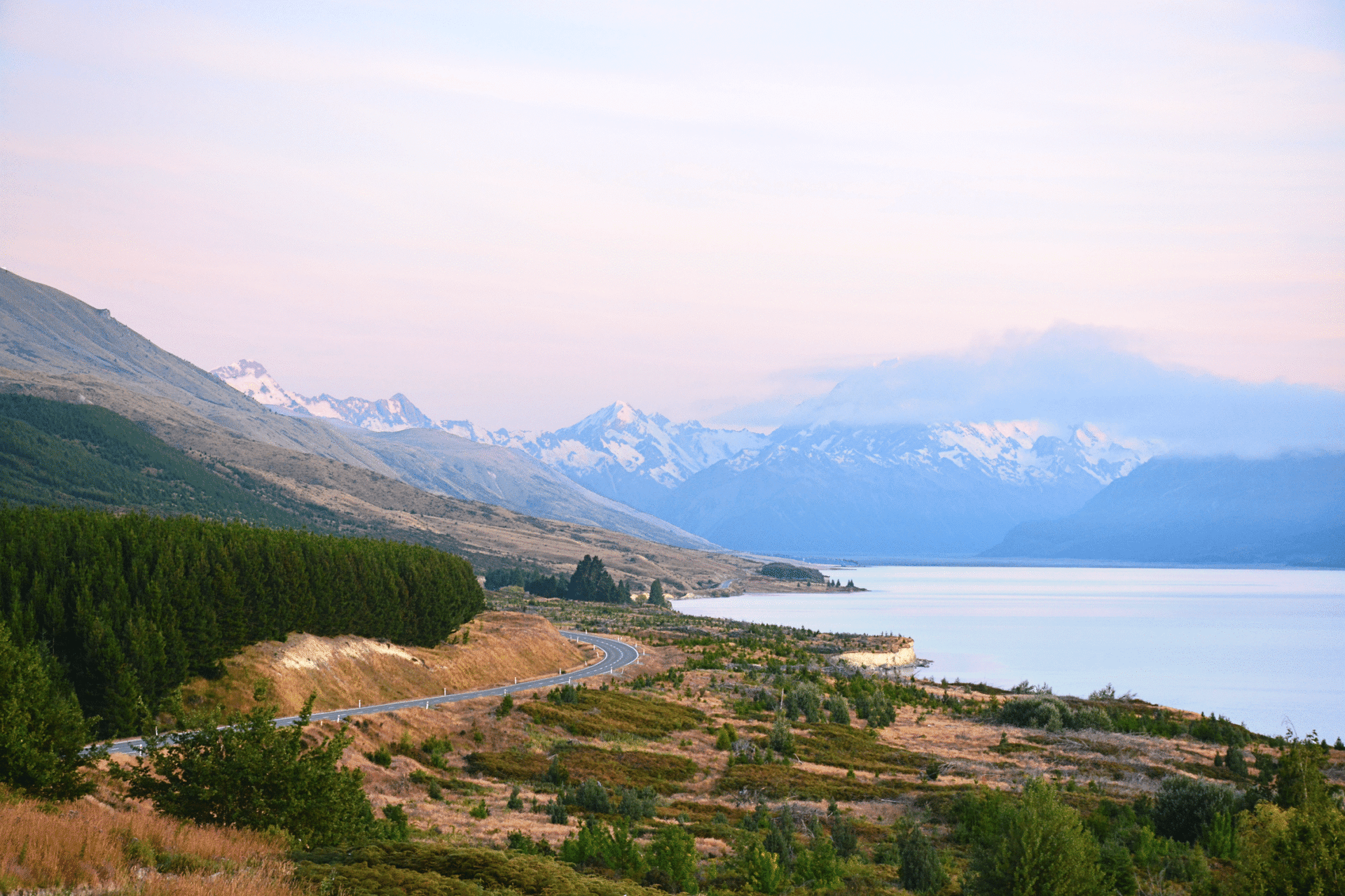 Picturesque landscape of Lake Pukaki with mountains and winding road at sunset in New Zealand.