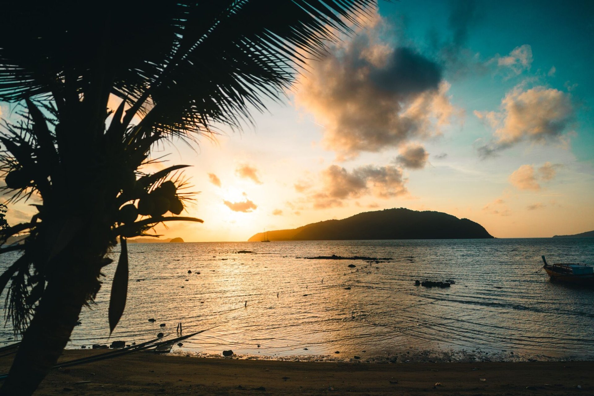 Stunning sunset view over a calm beach in Phuket, Thailand, with silhouetted palm tree and vibrant sky.