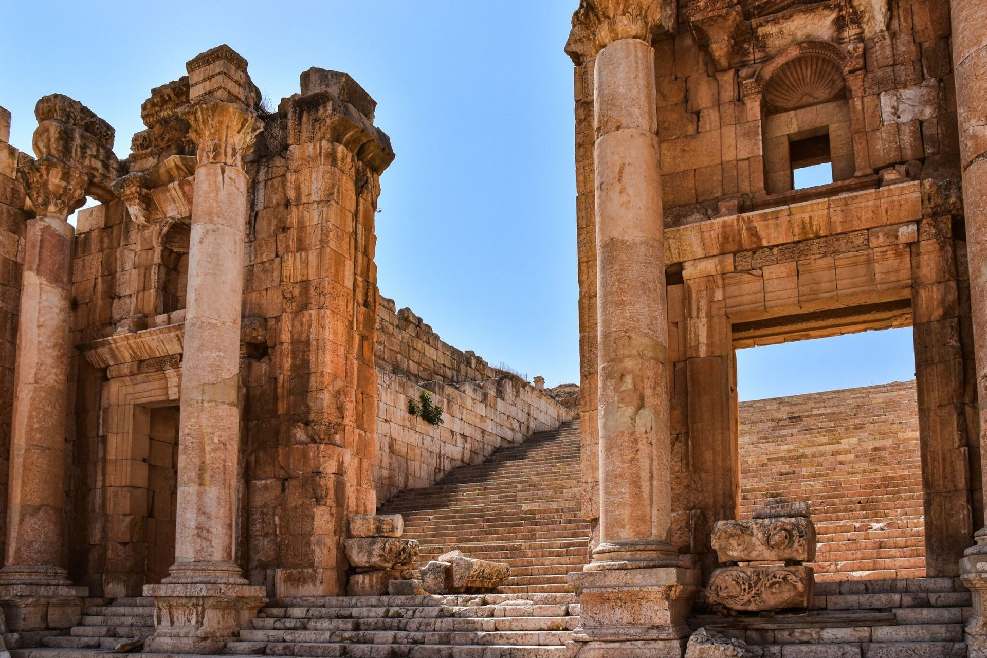 Explore the ancient ruins of Petra with stunning stone columns and stairs under a clear sky.