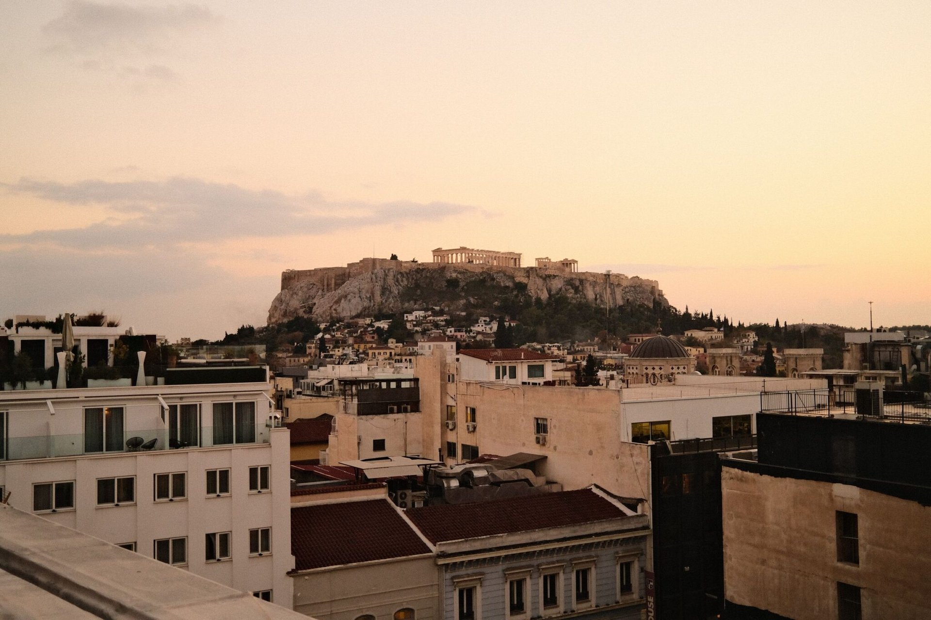 Scenic sunset view of the Acropolis in Athens, Greece, framed by city rooftops and a pastel sky.