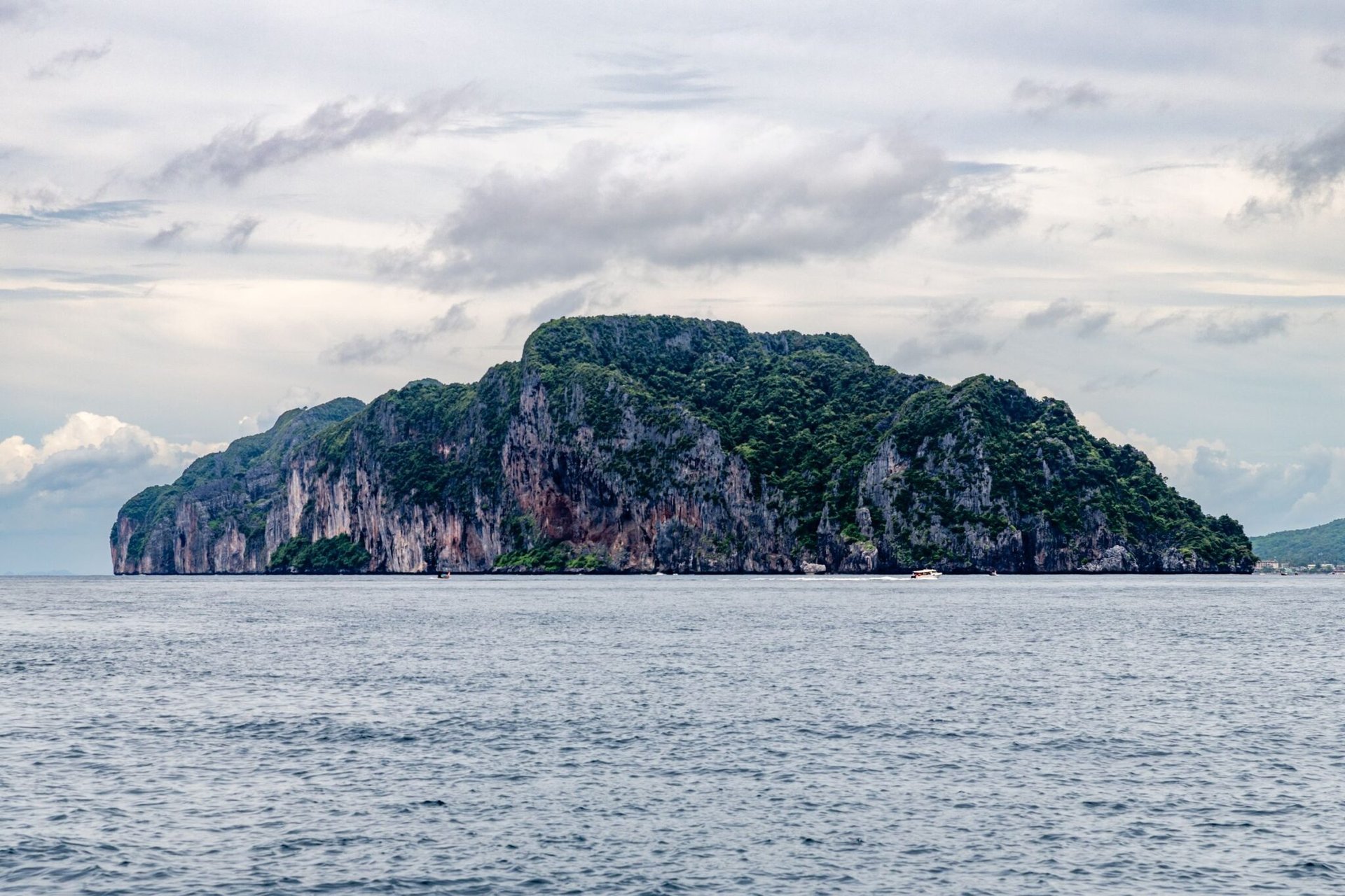 A breathtaking view of a rocky island cliff surrounded by the sea in Phuket, Thailand, under a cloudy sky.