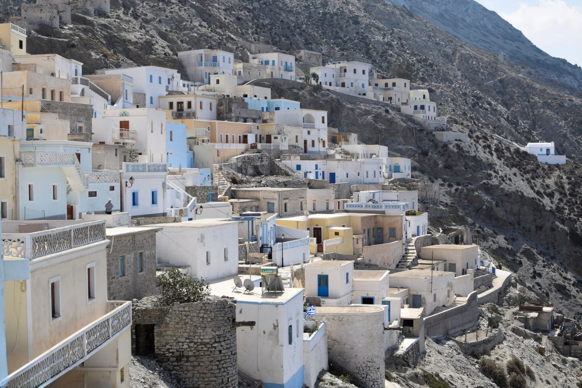 Charming Greek island village with whitewashed houses nestled into a rocky hillside, under a bright sky.