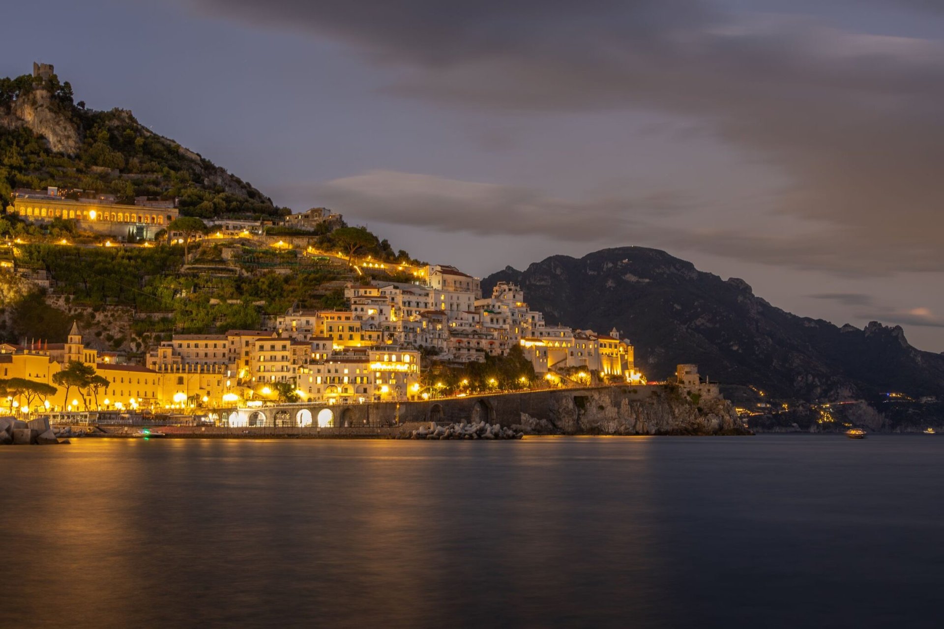 Stunning twilight view of the illuminated Amalfi Coast, Italy with calm waters.
