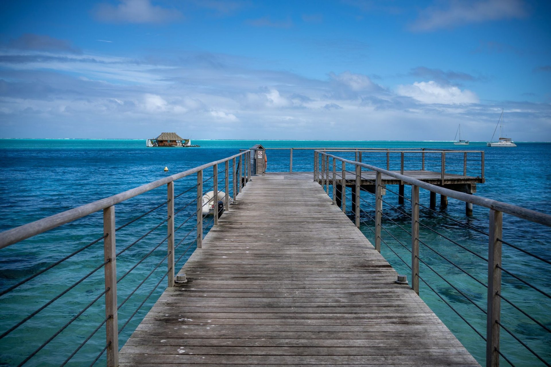 Peaceful view from a wooden dock extending over the turquoise waters of Polynesia with boats in the distance.