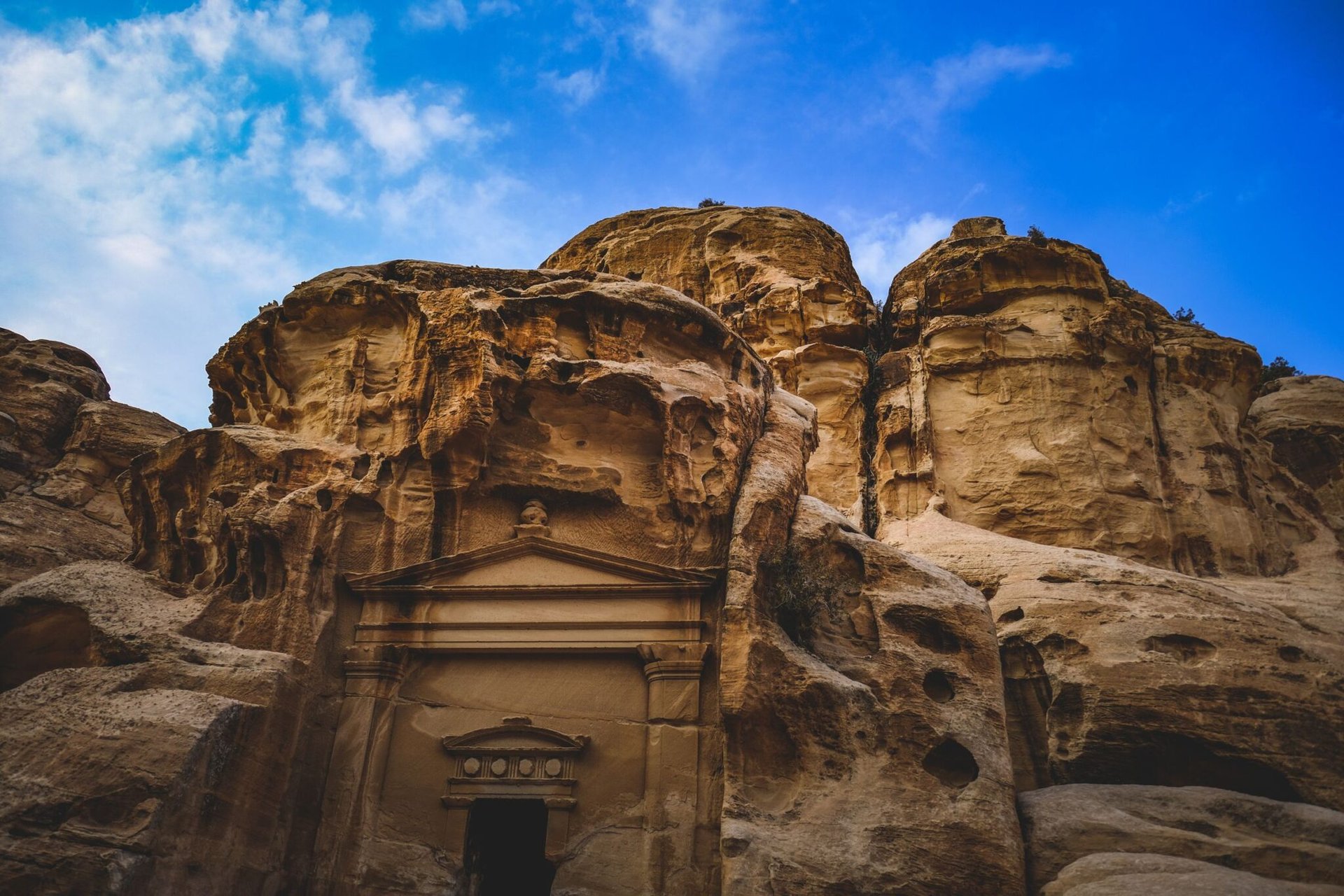 Explore the antiquity of Petra with this stunning image of a rock-carved triclinium against a vibrant blue sky.