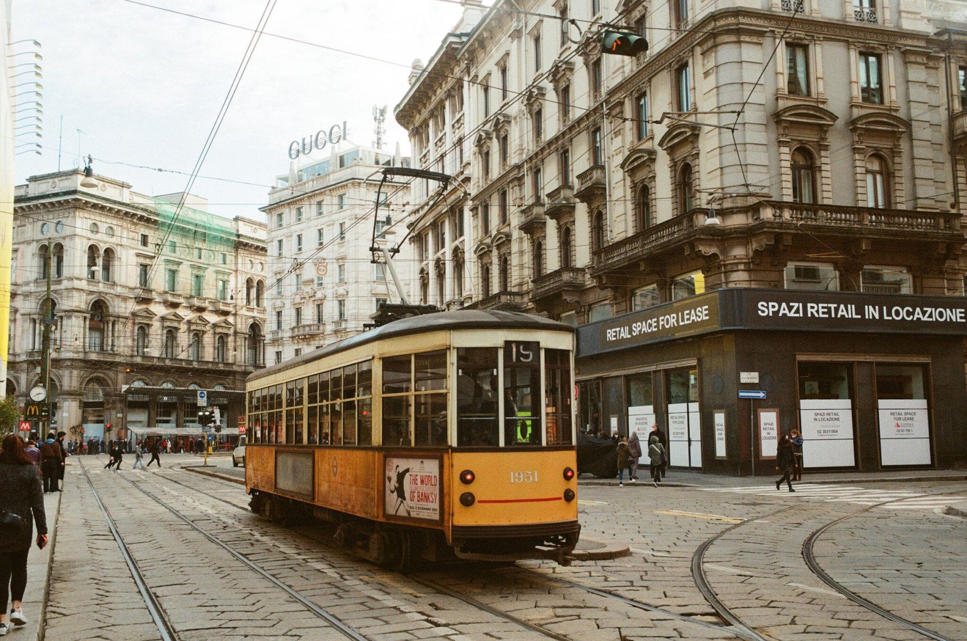 A vintage tram navigates the bustling streets of Milan, Italy, showcasing classic architecture.