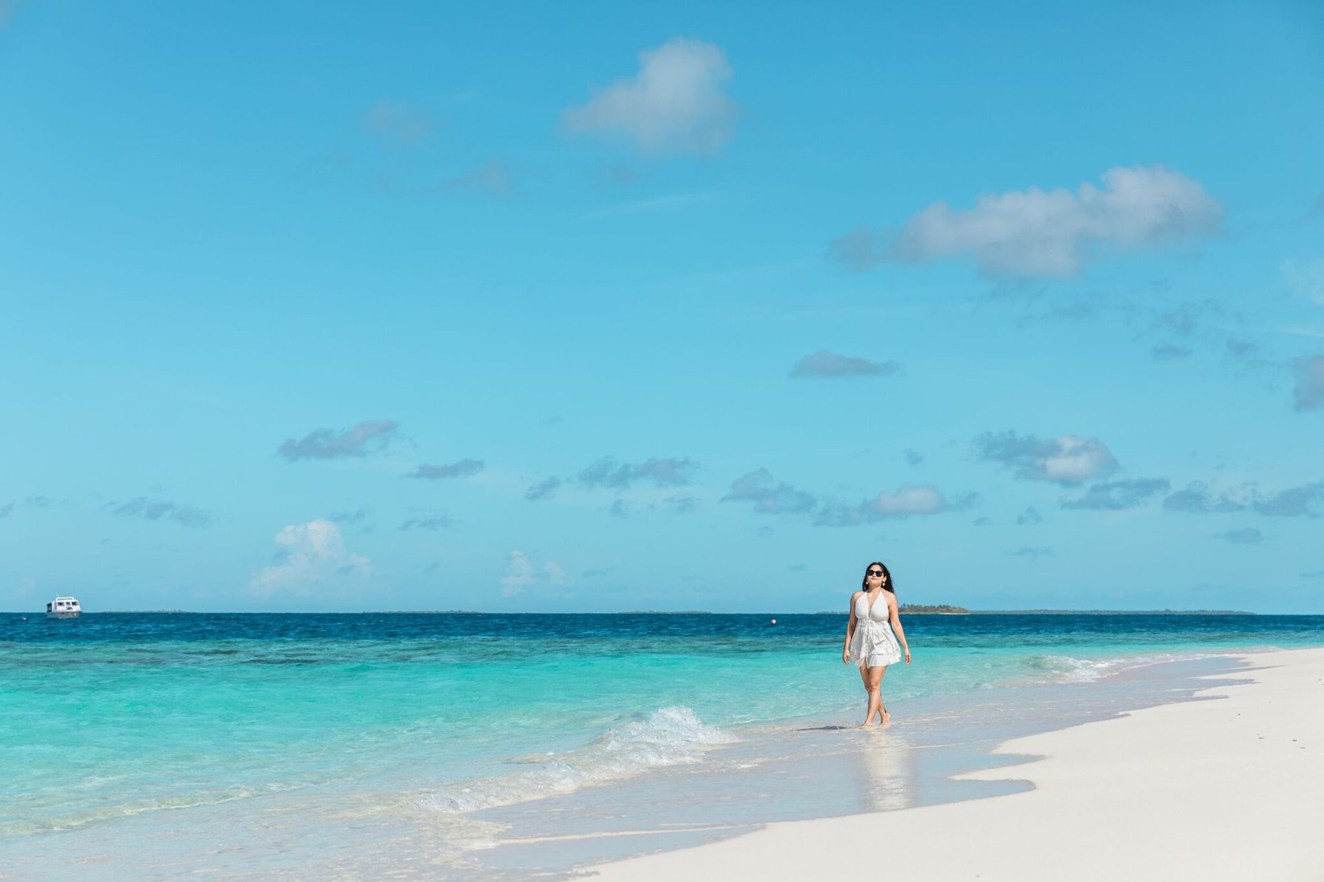 Woman walking along a beautiful white sandy beach in the Maldives under a bright blue sky.