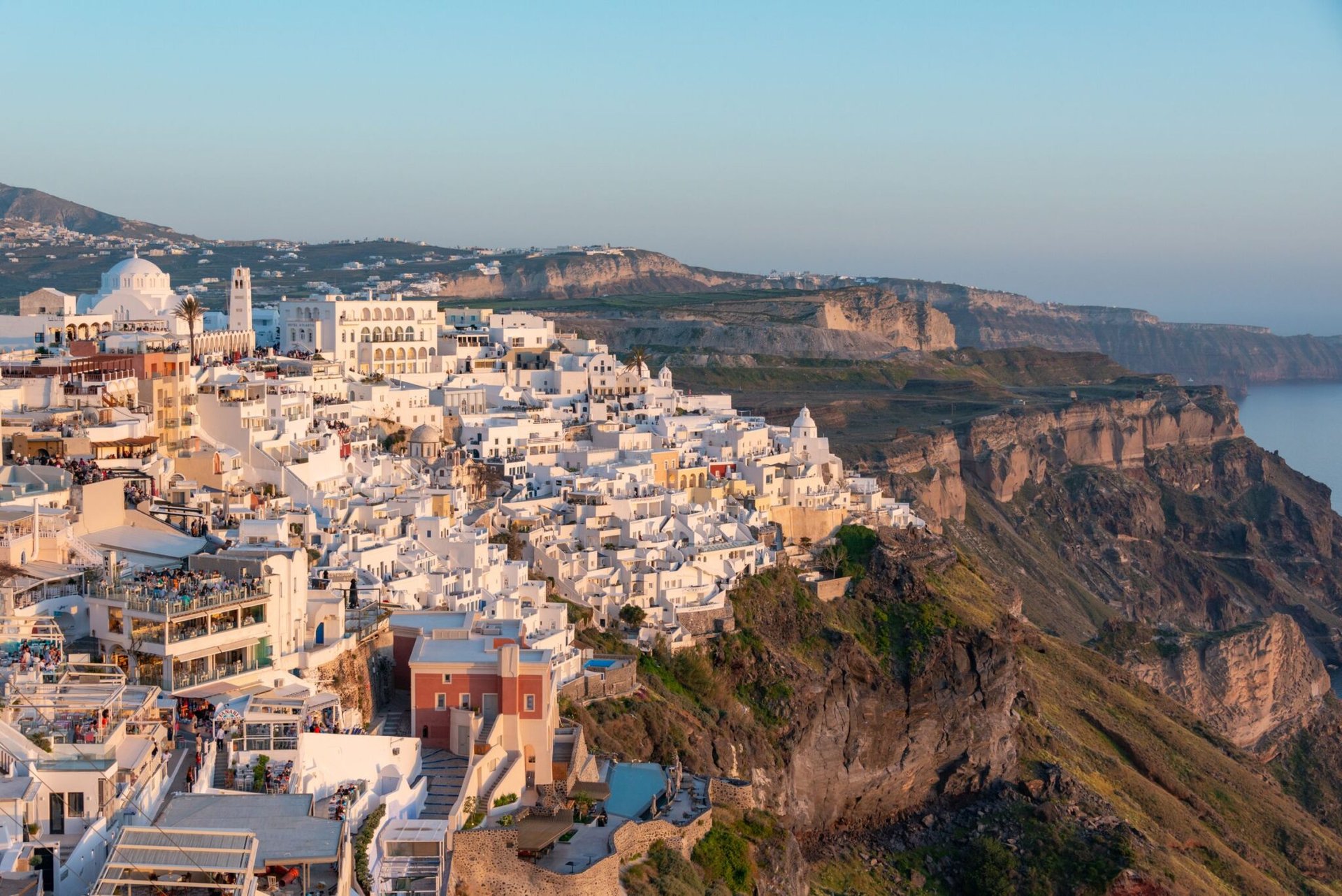 Spectacular aerial view of whitewashed buildings atop the cliffs of Santorini, Greece at sunset.