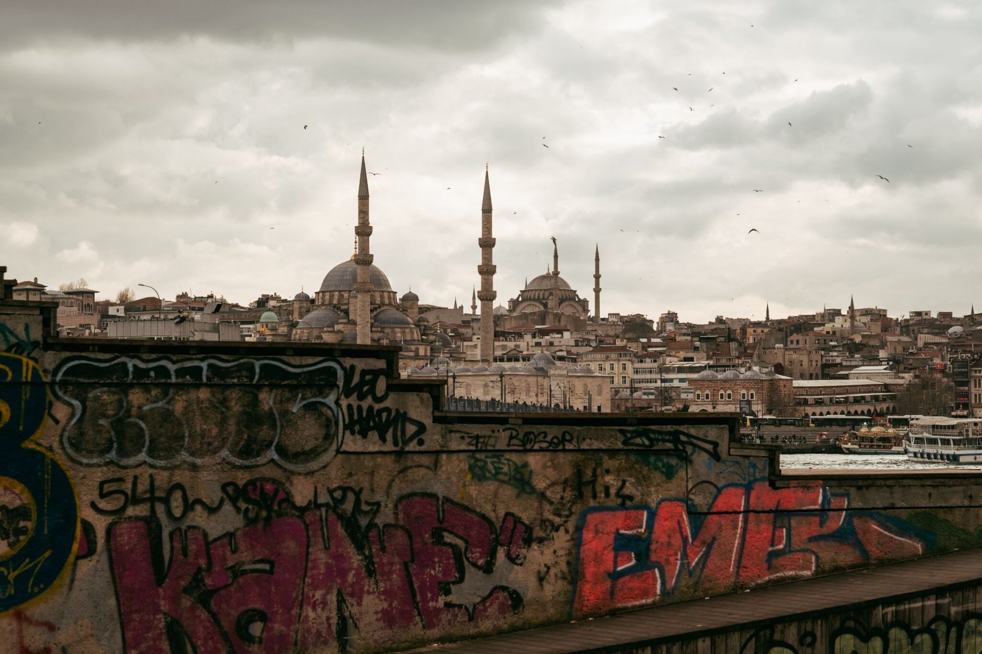 Graffiti-covered wall overlooking Istanbul skyline with iconic mosques on a cloudy day.