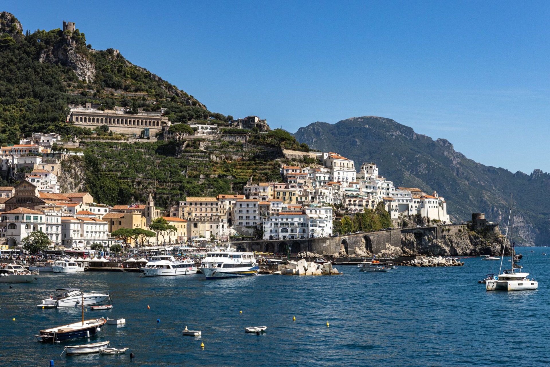Breathtaking view of Amalfi's coastal town and marina under a clear summer sky in Italy.