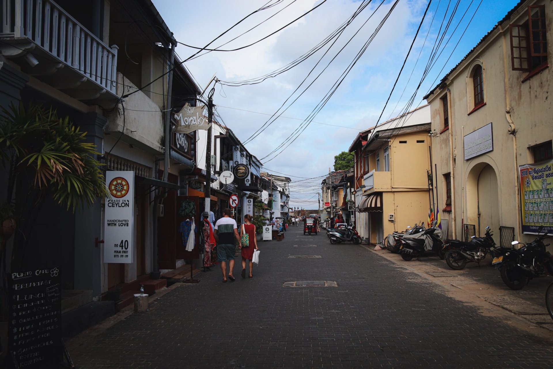 Historic street scene in Galle Fort, Sri Lanka with shops and pedestrians under a blue sky.
