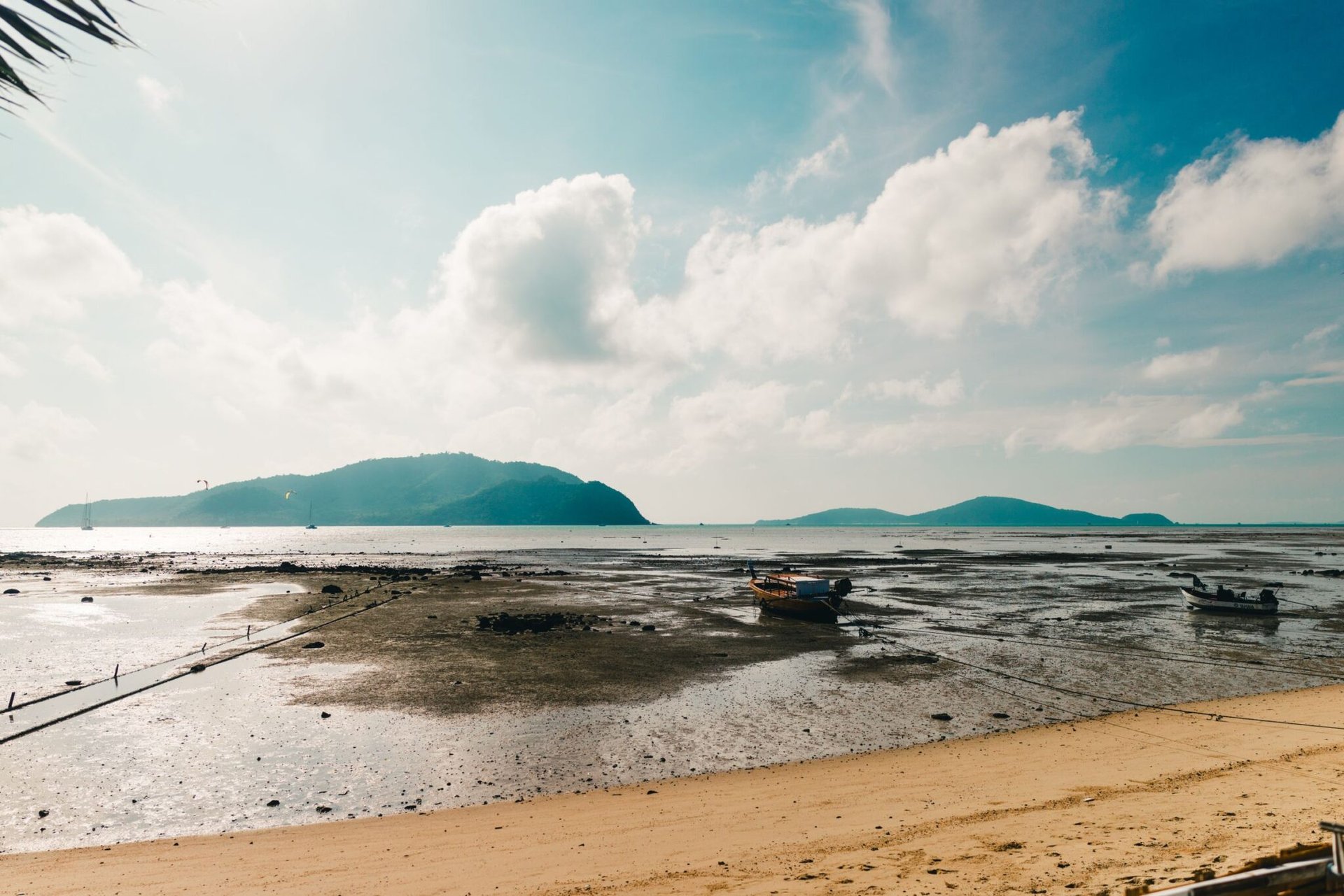Scenic view of a tranquil beach in Phuket, Thailand with boats and mountains in the background.