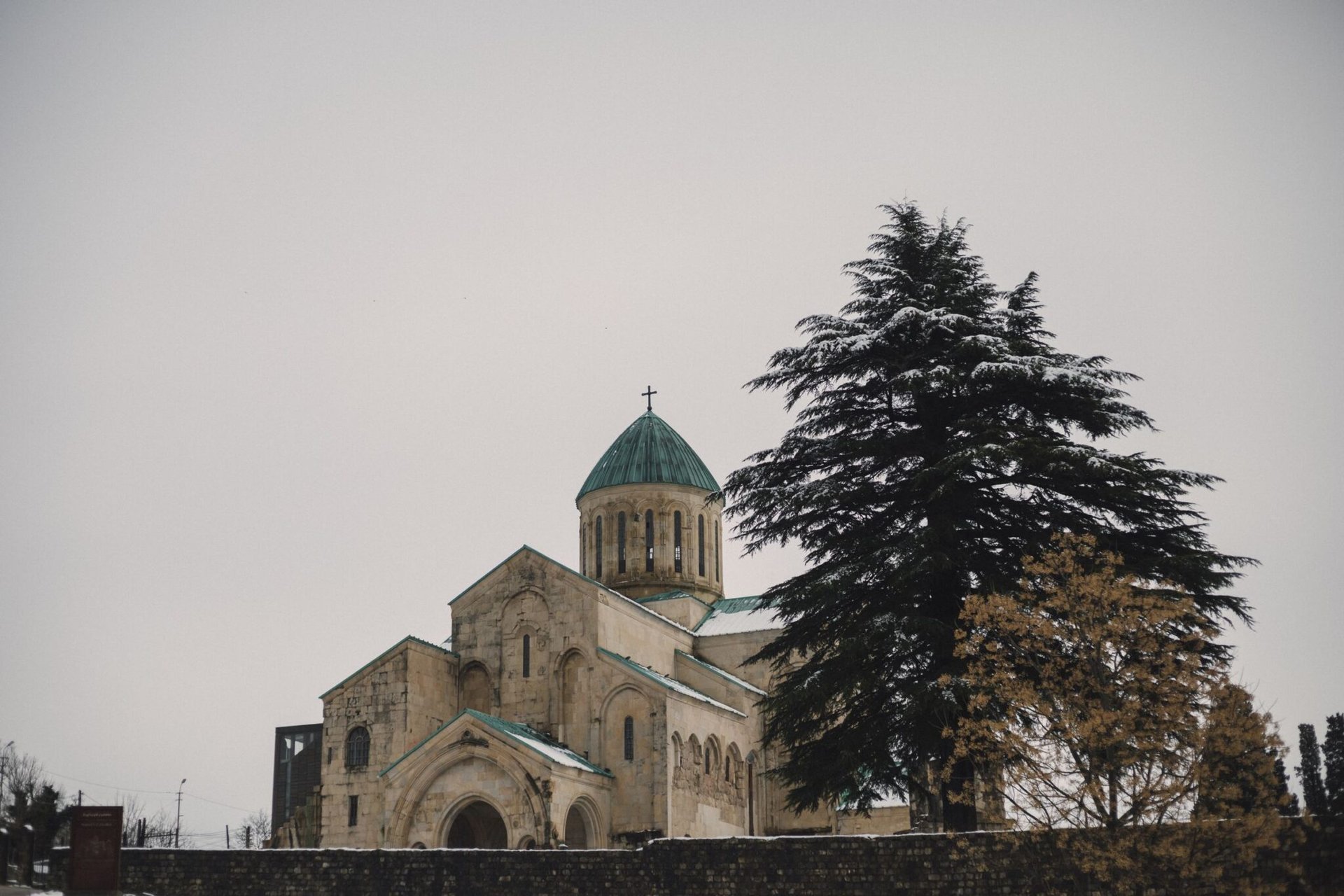A serene winter view of a historic cathedral in Tbilisi, Georgia with snow-covered trees.
