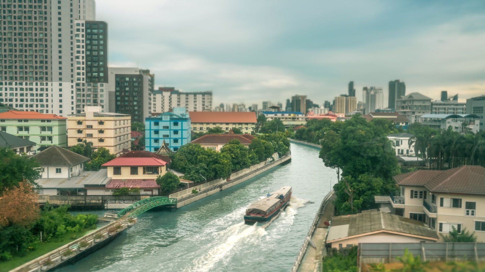 Peaceful canal scene with vibrant buildings and a boat in Bangkok, Thailand.