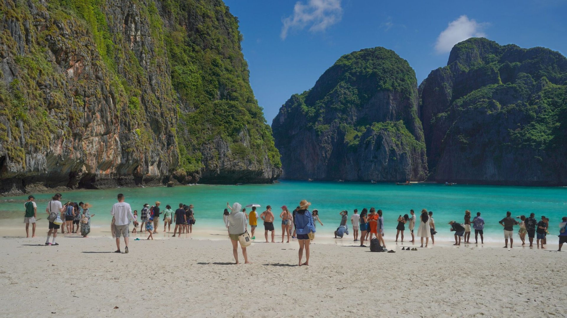 Visitors on the picturesque beach of Maya Bay in Thailand, surrounded by lush cliffs and turquoise waters.