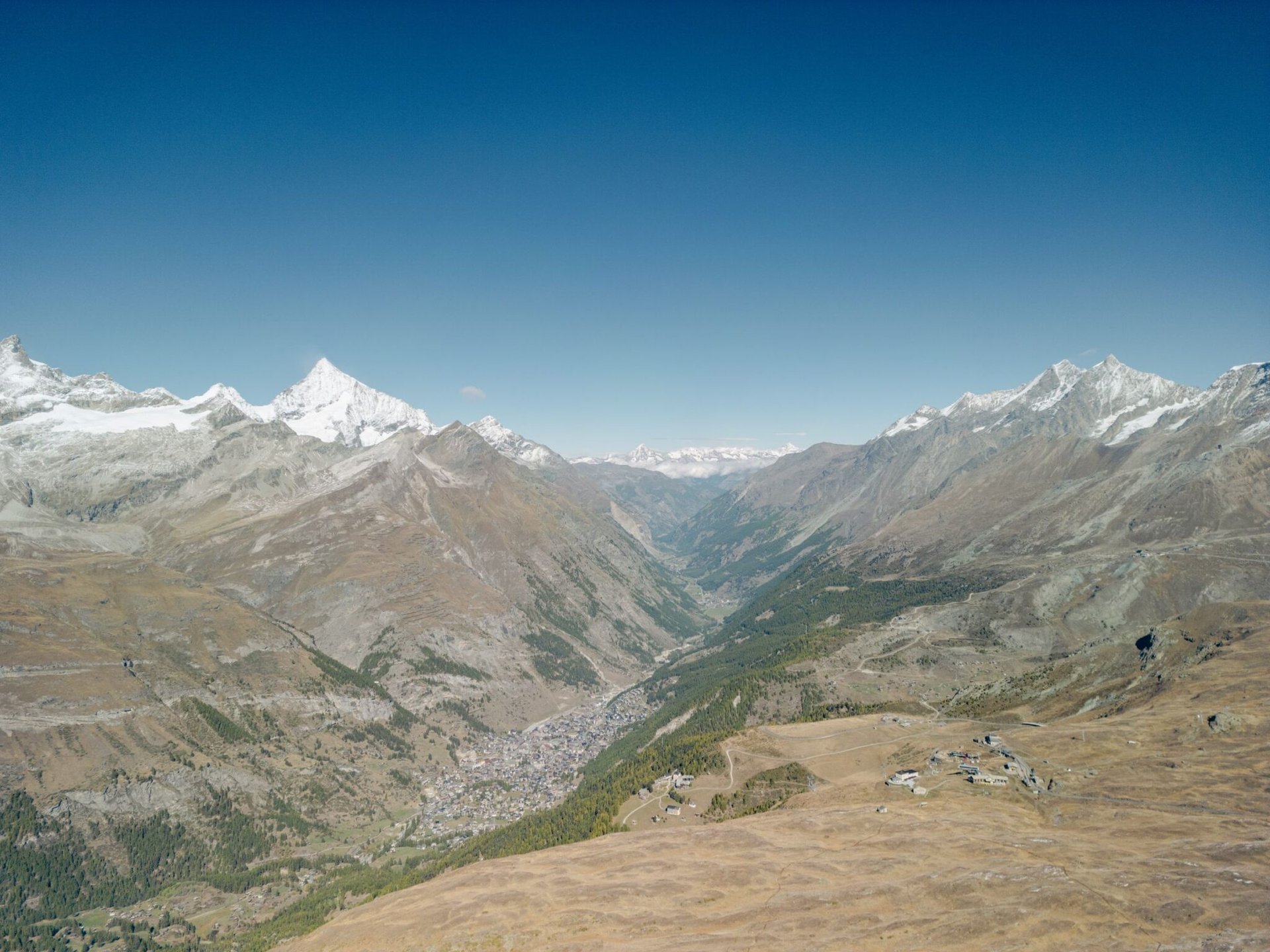 Idyllic aerial view over the Swiss Alps and Zermatt valley with snow-capped peaks under a clear blue sky.