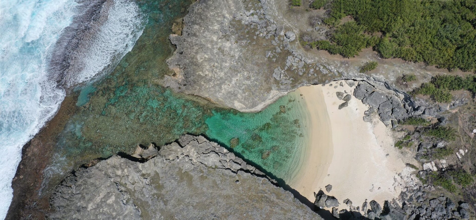Stunning aerial shot of a secluded beach cove in Rodrigues, Mauritius, showcasing clear turquoise waters and rugged coastline.